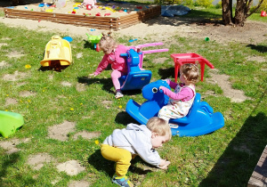 dzieci w piaskownicy, dwie dziewczynki na bujakach, chłopiec klęka na trawie