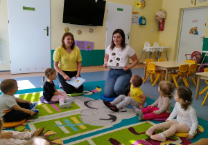 dzieci wraz z opiekunkami siedza na dywanie, opiekunka pokazuje bluzkę na której ma narysowane pszczoły
