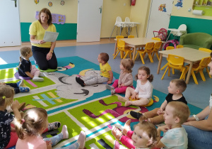 wszyscy siedzą na dywanie i słuchają czytanego przez opiekunkę wiersza
