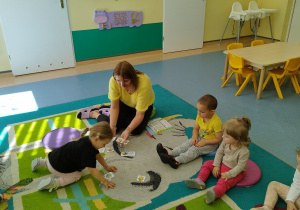 dziewczynka wybiera obrazek spośród tych na dywanie, wszyscy siedzą i patrzą