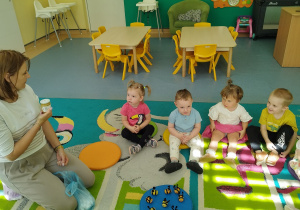 wszyscy siedzą na dywanie, opiekunka pokazuje słoik z miodem
