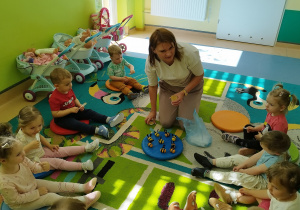 opiekunka z dziećmi na dywanie, trzyma słoiczek miodu, częstuje dzieci