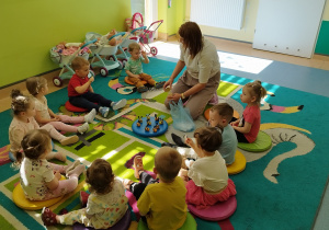 dzieci siedzą na dywanie , niektóre mają łyżeczki z miodem, opiekunka patrzy