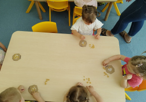 dzieci przy stoliku przyklejają makaron do tekturek