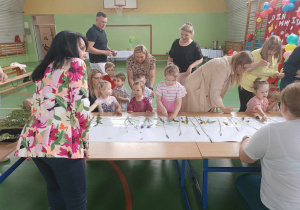 dzieci i rodzice przyklejają do kartonu trawy i kwiaty, pani dyrektor się przygląda