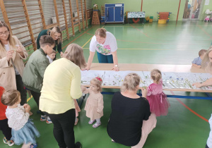 dzieci i rodzice wokół kartonu przyklejają trawy i kwiaty
