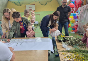 dzieci wraz z rodzicami przyklejają trawy i kwiaty do kartonu