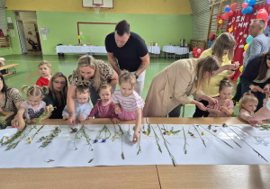 dzieci wraz z rodzicami tworzą pracę plastyczną przyklejają trawy