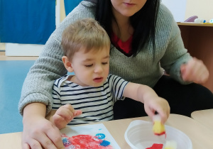 chłopiec maluje gąbką, z tyłu siedzi opiekunka