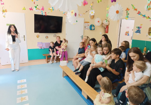 rodzice z dziećmi siedzą na ławkach, słuchają przemówienia pani dyrektor