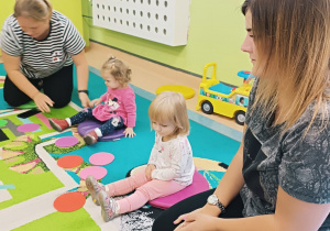 opiekunki i dzieci siedzą na dywanie , przed nimi leżą kolorowe kropki