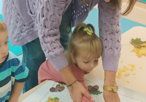 opiekunka pomaga dziewczynce nakleić liść