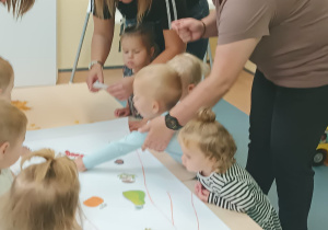 opiekunki pomagają dzieciom naklejać obrazki na kartonie