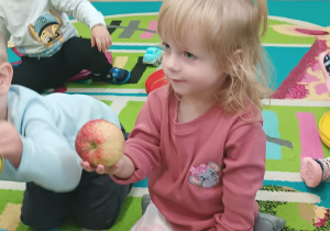 dziewczynka trzyma i pokazuje jabłko