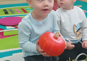 chłpiec uśmiecha się , trzyma w rękach pomarańczową dynię
