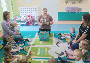 wszyscy siedzą na dywanie, opiekunka czyta wiersz