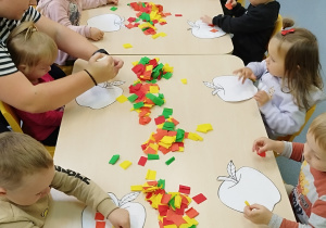 dzieci kleją bibułę, opiekunka pomaga dziecku