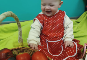 dziewczynka siedzi , uśmiecha się, przed nią stoi kosz z jabłkami
