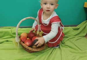 chłopiec kuca obok stoi kosz z jabłkami