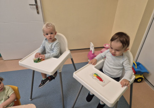 chłopcy siedzą w krzesłach , jeden gniecie woreczek , a drugi patrzy