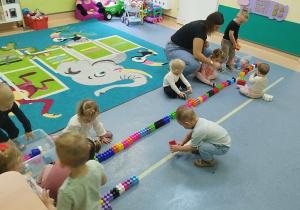dzieci układają klocki na liniach na podłodze, opiekunka pomaga dzieciom