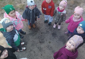 dzieci stoją w kole, niektóre patrzą w aparat