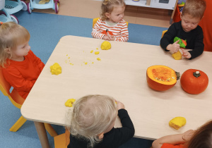dzieci siedzą przy stoliku , ugniatają masę dyniową