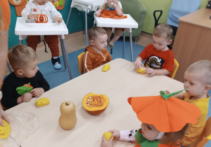 dzieci siedzą przy stoliku i bawią się masą dyniową