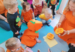 opiekunka pokazuje dzieciom siedzącym obok niej co dynia ma w środku