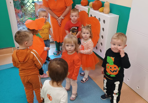 opiekunka opowiada dzieciom stojącym wokół niej o dyniach