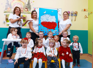 żlobkowe dzieci i opiekunki pozują do zdjęcia trzymając wspólnie wykonaną pracę plastyczną