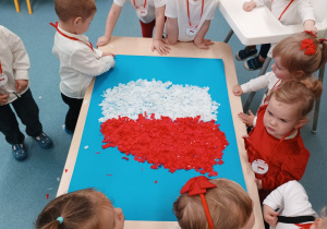 dzieci stoją wokół stolika, na którym leży wyklejony kontur mapy Polski