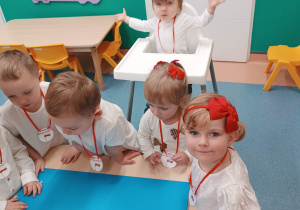 dzieci stoją wokół stolika , wykonują pracę plastyczną