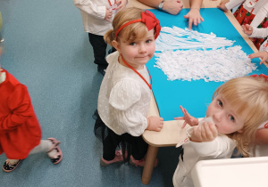 dzieci stoją wokół stolika, opiekunka smaruje karton klejem