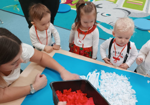 opiekunka rozdaje dzieciom czerwoną bibułę