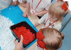 opiekunka rozdaje dzieciom czerwoną bibułę