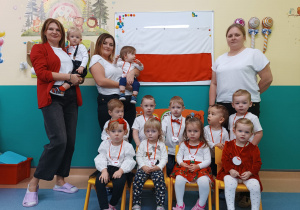 dzieci i opiekunki pozują do zdjęcia z flagą Polski