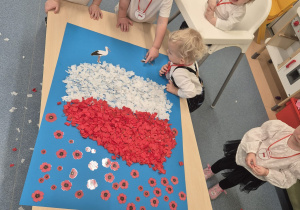 dzieci przyglądają się wykonanej pracy plastycznej, i doklejają bociany