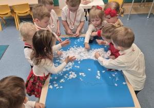 dzieci stoją wokół stolika wyklejają kontur Polski białą bibułą