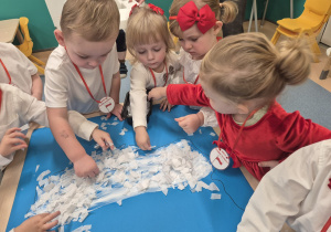dzieci przyklejają biała bibułę , na karton