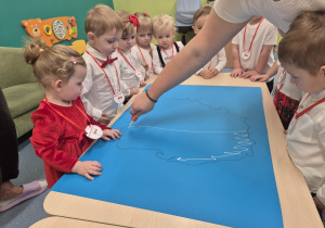 dzieci patrzą, opiekunka smaruje klejem katron