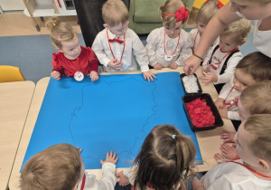 dzieci stoją wokół stolika, na którym leży narysowany na kartonie kontur mapy Polski