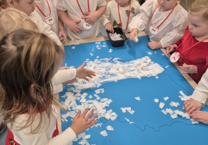 dzieci stoją wokół stolika i wyklejają białą bibułą, kontur mapy Polski