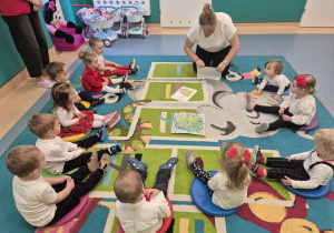 dzieci siedzą na dywanie, opiekunka pokazuje ilustracje z symbolami Polski