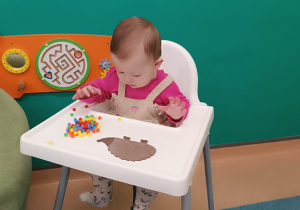 dziecko siedzi , przed nim lezy jeż i kolorowe kulki