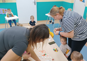 opiekunki pomagają dzieciom siedzącym przy stoliku w wykonaniu pracy