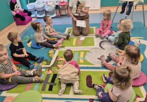 dzieci siedzą na dywanie, opiekunka czyta im wiersz