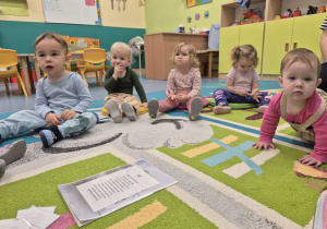 dzieci siedzą na dywanie, słuchają opiekunki
