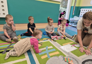 dzieci siedzą na dywanie słuchają wiersza czytanego przez opiekunkę