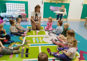 dzieci siedząc na dywanie słuchają czytanego przez opiekunkę wiersza